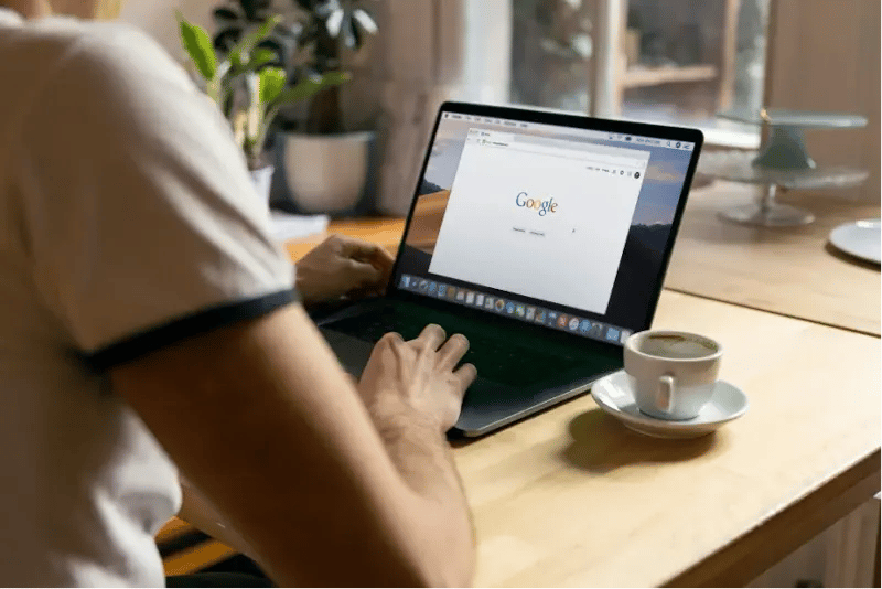 Mann mit Kaffeetasse sitzt vor Laptop