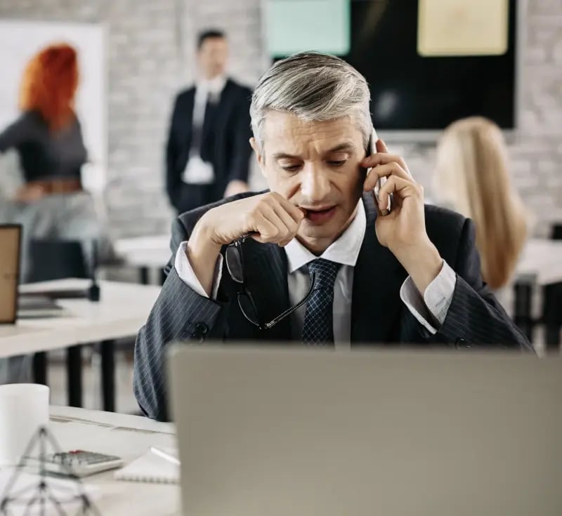 Thoughtful man at laptop with cell phone in hand