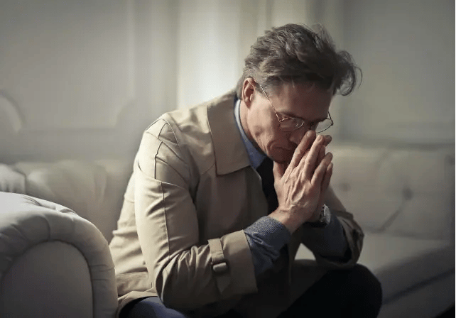 Ein Mann in einem Trenchcoat mit den Händen vorm Gesicht